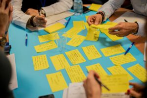 Deelnemers in een brainstorm sessie met geschreven gele stickynotes op een fel blauwe ondergrond