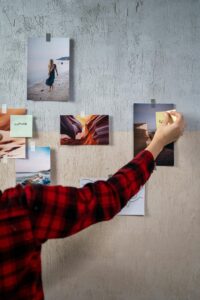 Persoon in een rood-zwart geblokt overhemd die diverse foto's en woorden op de muur plakt